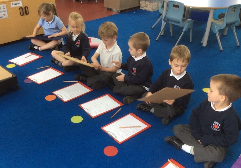 a line of pupils sit cross legged on the floor and complete their science work