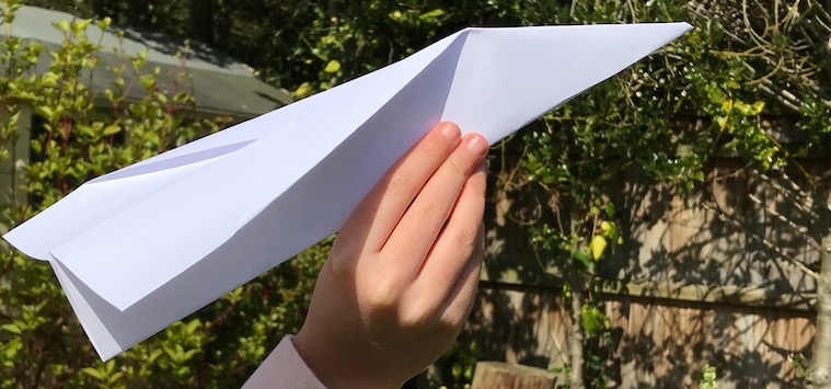 A close up of a hand preparing to throw a paper aeroplane