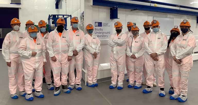 a large group in white protective clothing and orange hard hats