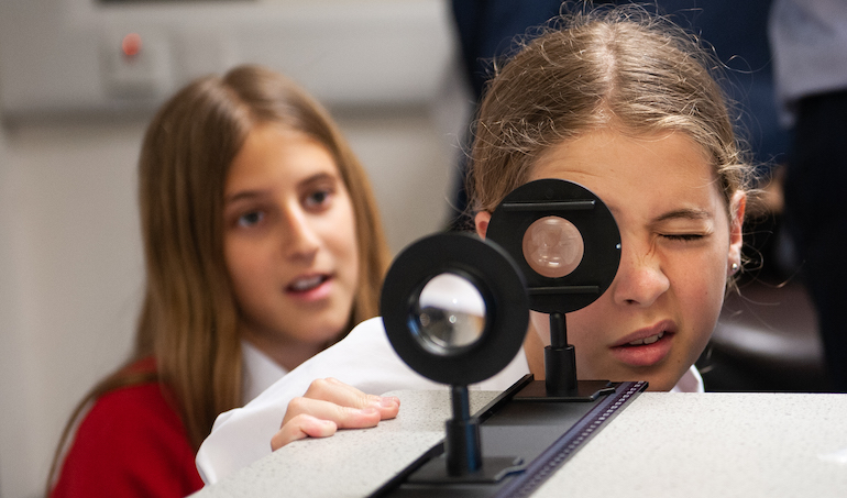 two girls - one looking through a magnifying eye piece