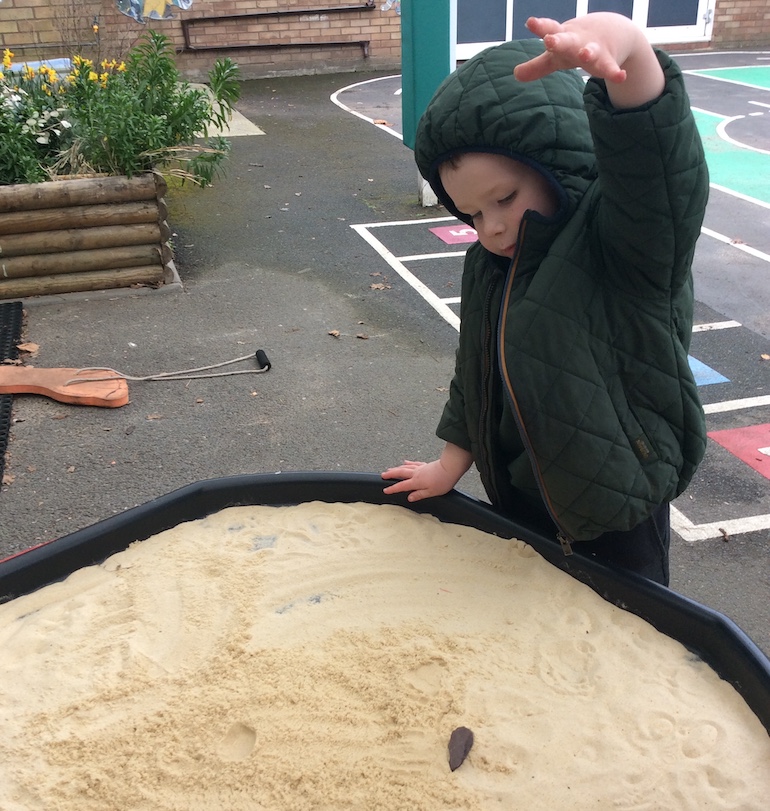 child drops a stone into a sandpit