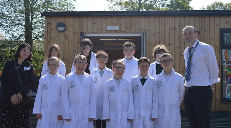 a group of children in lab coats are pictured in a group outside with two grown ups