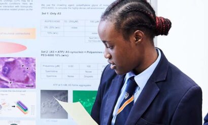A student female is looking at a sheet of paper along with a poster behind her with science facts.
